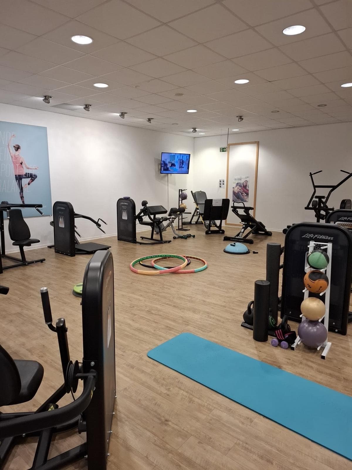 Die Trainingsfläche mit Kraftgeräten an der Wand, drei bunten Hula-Hoop-Reifen auf dem Holzboden und einer türkisen Gymnastikmatte im Vordergrund.